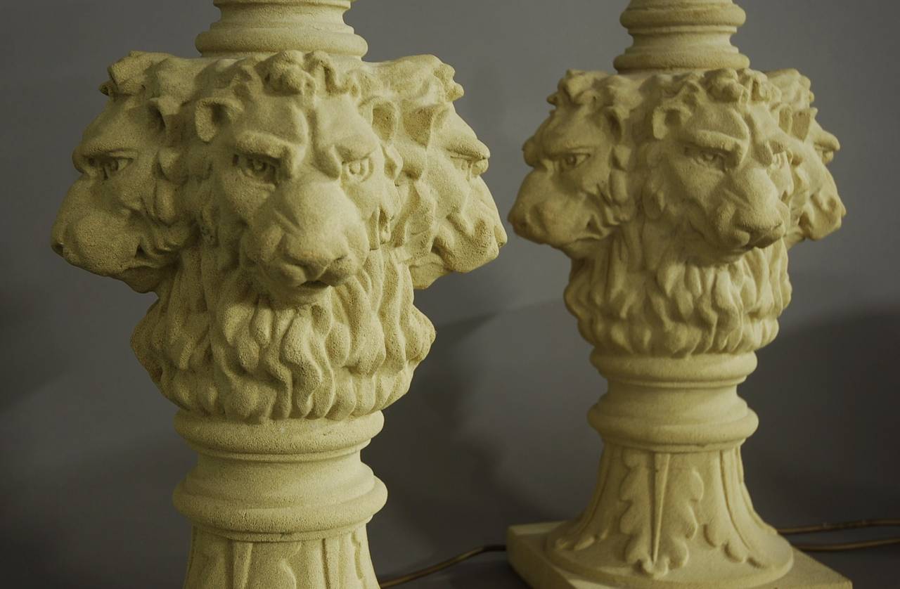 A large pair of reconstituted sandstone lions head table lamps.

The lamps consists of a lions head on each side leading down to leaf decoration with a square base.

The lamps have been photographed with neutral shades (from Laura Ashley) for