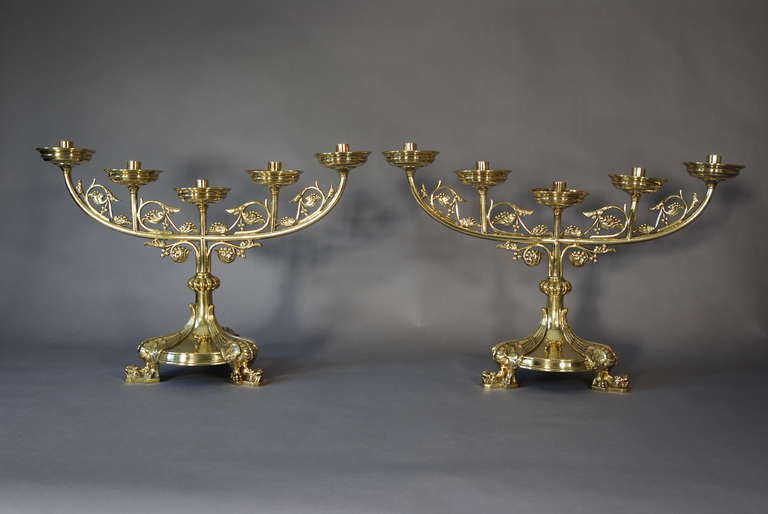 A very good pair of mid-20th century large Gothic style five branch brass candlesticks. 

These consist of five candleholders with drip trays and between these scrolls of foliage decoration. 

These lead down to a central stem with a ball style