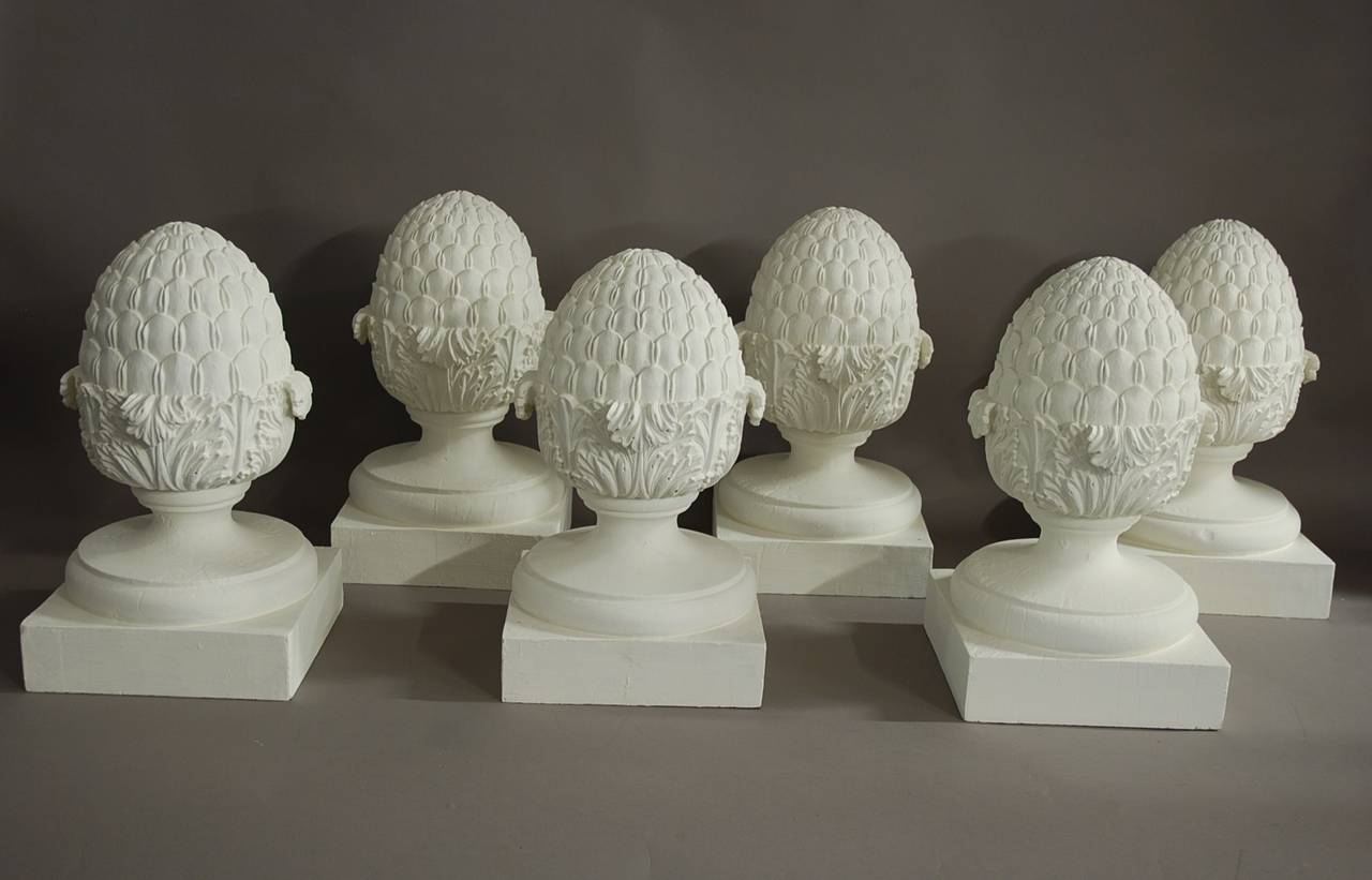 A highly decorative set of six early 20th century carved wooden pineapple finials painted in an off-white finish.

They consist of a carved pineapple with scrolled foliage and a turned circular stand leading down to a square base.

These