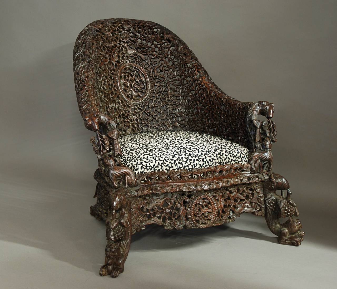 A highly decorative mid 19th century profusely carved hardwood armchair from the Bombay area of India of superb quality.

This chair consists of a profusely carved and pierced arched back depicting animals and foliage with a central oval panel