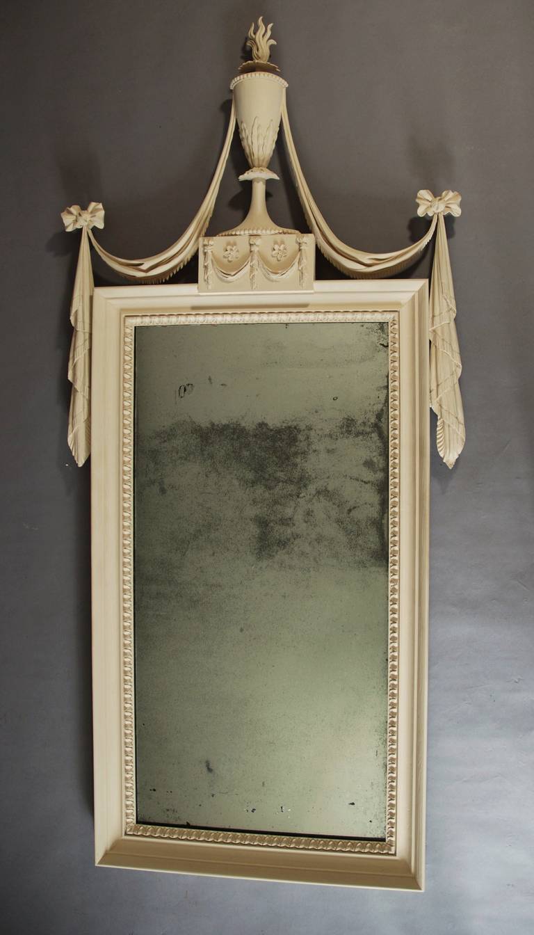 A highly decorative finely carved 19th century pine mirror in the Adam style with a light cream finish.
 
The mirror consists of a finely carved urn with flamed finial with swags and bows to the top with an oblong panel of drapery and carved