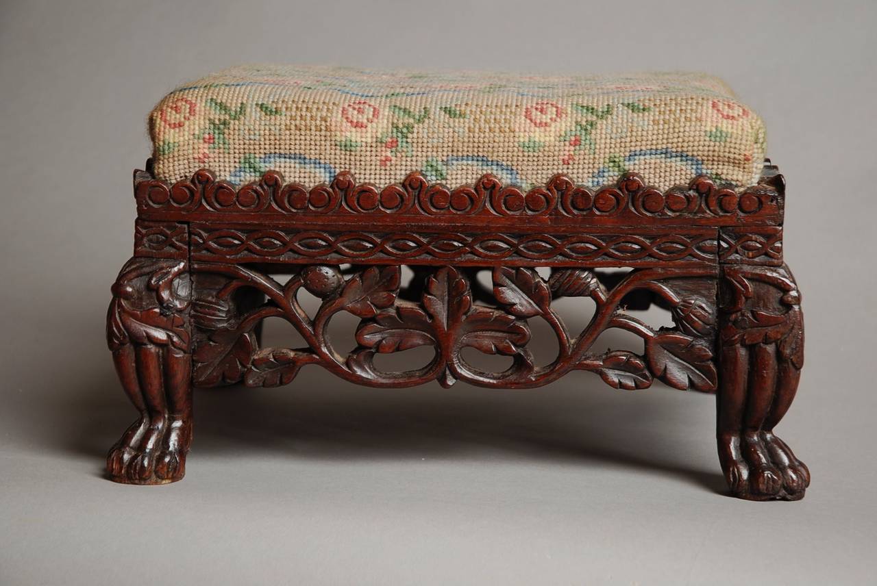 A late 19th century Anglo Indian carved padouk foot stool.

The top is upholstered with a needlework fabric which can be easily re-upholstered by the purchaser if necessary.

The base is very decorative with carved & shaped rails with