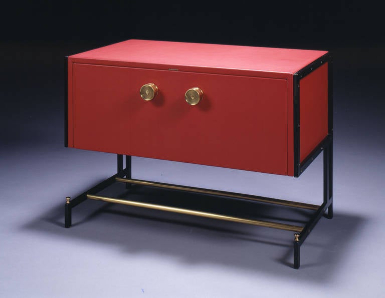 Little bar of a quadrangular shape, raising on a blackened metal frame and two brass stretchers. Opening on its front on a hinged slop and brass rings. Re-upholstered with red leather.
circa 1938.