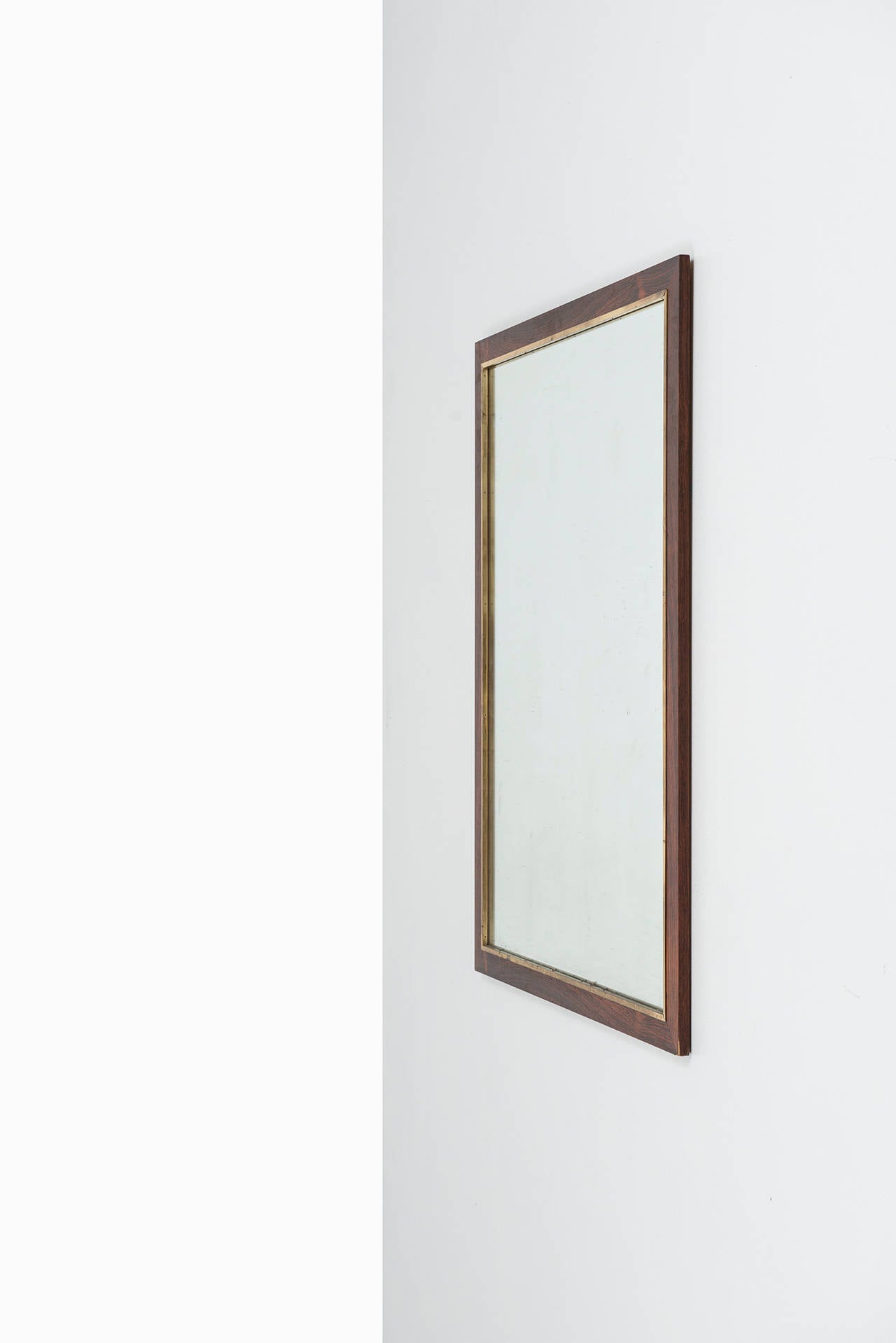 A large rosewood mirror with brass detail. Produced by Fröseke, AB Nybrofabriken in Sweden.
