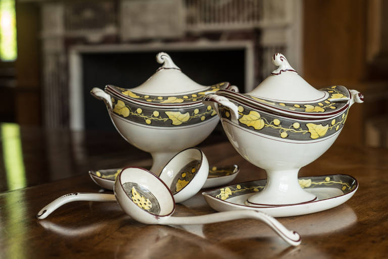 A very rare, beautiful and undamaged pair of Davenport creamware sauce tureens and covers. One with its ladle and one with sifter spoon. Painted with a border pattern of repeated yellow leaf and three-fruit motif on a grey-green ground within a