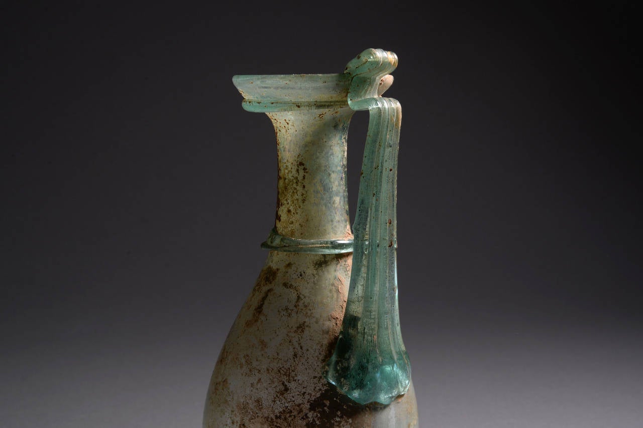 A beautiful, large Roman glass oinochoe or jug, dating from the 2nd to the 4th century AD.

Free blown of light green glass in one of the most elegant and refined ancient glass vessel shapes. The piriform body sits upon a ring base, and the