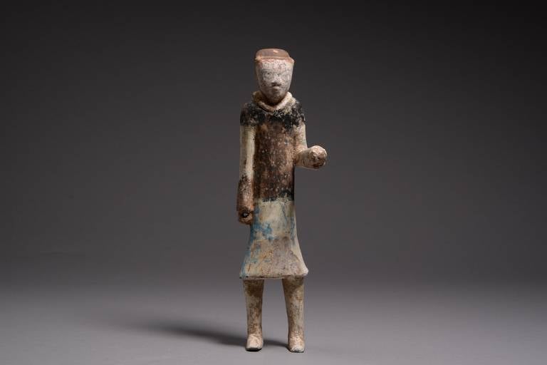 An ancient Chinese Han dynasty terracotta attendant figure, dating to 206 BC–220 AD.

Shown standing upright with elongated limbs, oval face and schematic features. He wears a suit of scale armour and a long tunic, with thick collar. The left arm