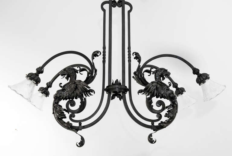Inspired by lamps of Middle Ages and the Renaissance, this wrought iron chandelier with four arms of light is articulated with scrolls from the main supported. Two dragons back to back escape from foliage scrolls and acanthus leaves. This prodigious