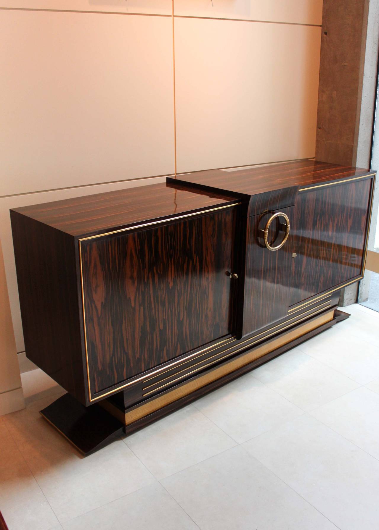 A fantastic example of the genre, this art moderne sideboard is completely original. Two lockable cabinets with deco keys flank a pull-out storage compartment for bottles. The impressive circular center handle resembling jewelry serves as the main
