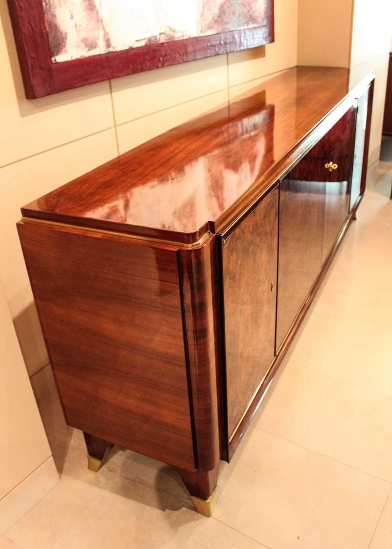 A stunning example of classic 1930s design, a burled walnut sideboard in the style of famed French cabinet maker Jules and André Leleu. Four lockable burled walnut doors open to expose a large central storage area with two drawers and six shelves,