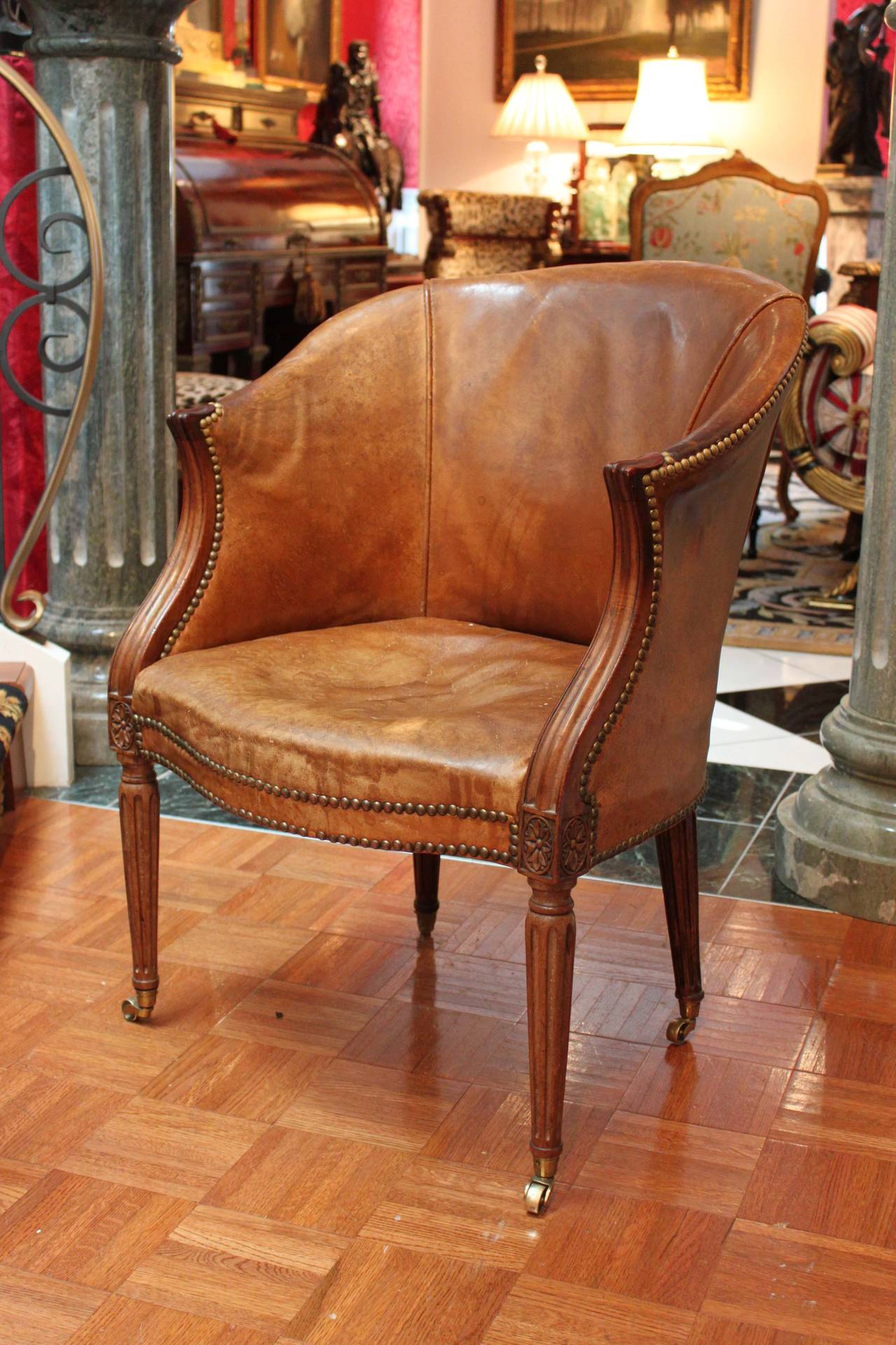 Carved mahogany desk chair in the Sheraton style, circa late 18th century. This chair retains it's original BADA seal and what may be it's original leather upholstery. Decorative rosette and fluted legs on brass castors.