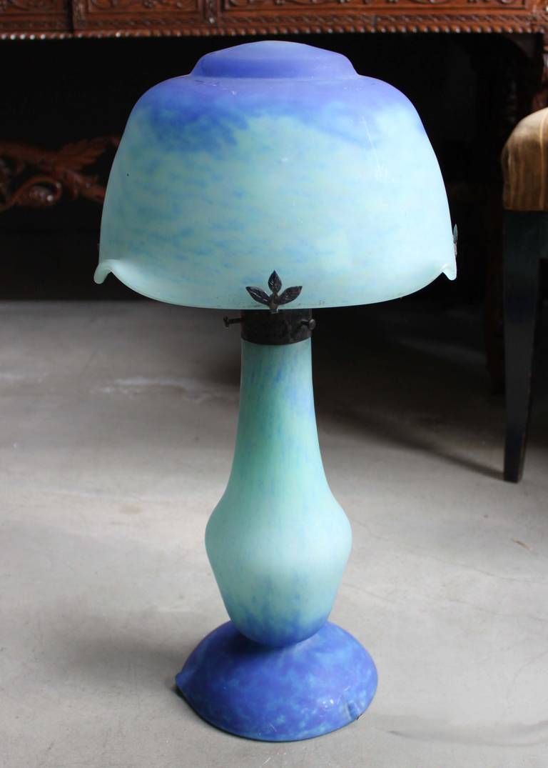 A stunning example of Daum glasswork, this early 20th century table lamp is crafted with a domed shade and baluster shaped base with a hand-hammered neck. Hues of cobalt blue and aquamarine transition throughout the base and shade. Signed Daum.
