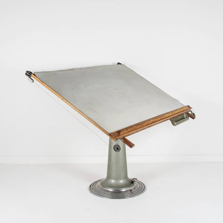 A stunning 1930s drafting table by Swedish manufacturer Nike Eskilstuna. A fully functional table with parallel rule, tool/pencil tray and foot adjustment. Minimalist form with a beautiful industrial-age pedestal in metallic hues of pewter and