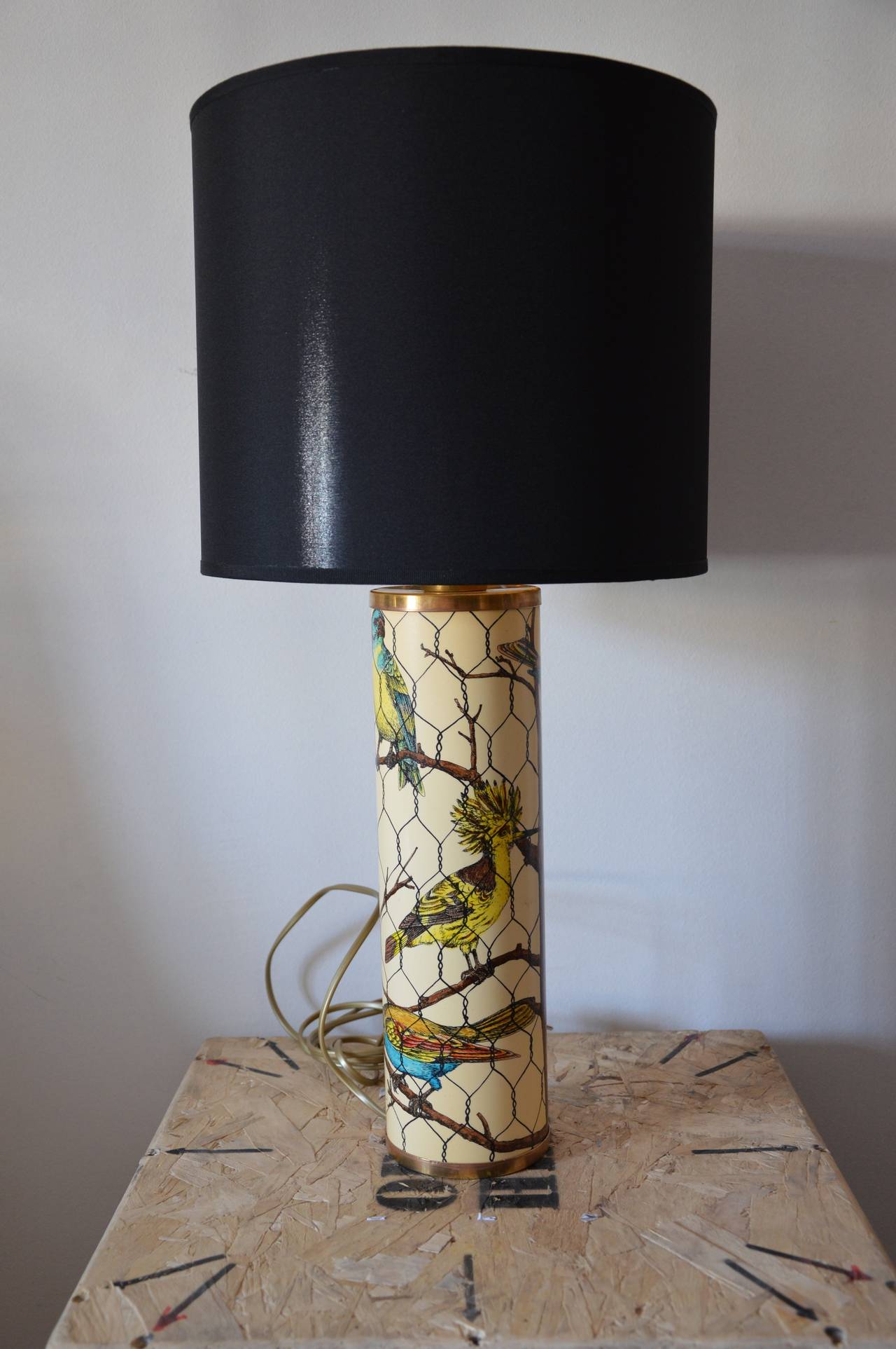 White cream table lamp by Piero Fornasetti with decor of birds. 
Base in brass with black clothe lampshade golden inside. Signed Fornasetti Milano on the bottom. 
Dimensions : 
H : 43cm 
Diameter : 10cm
H lamp + lampshade : 64cm
Diameter of