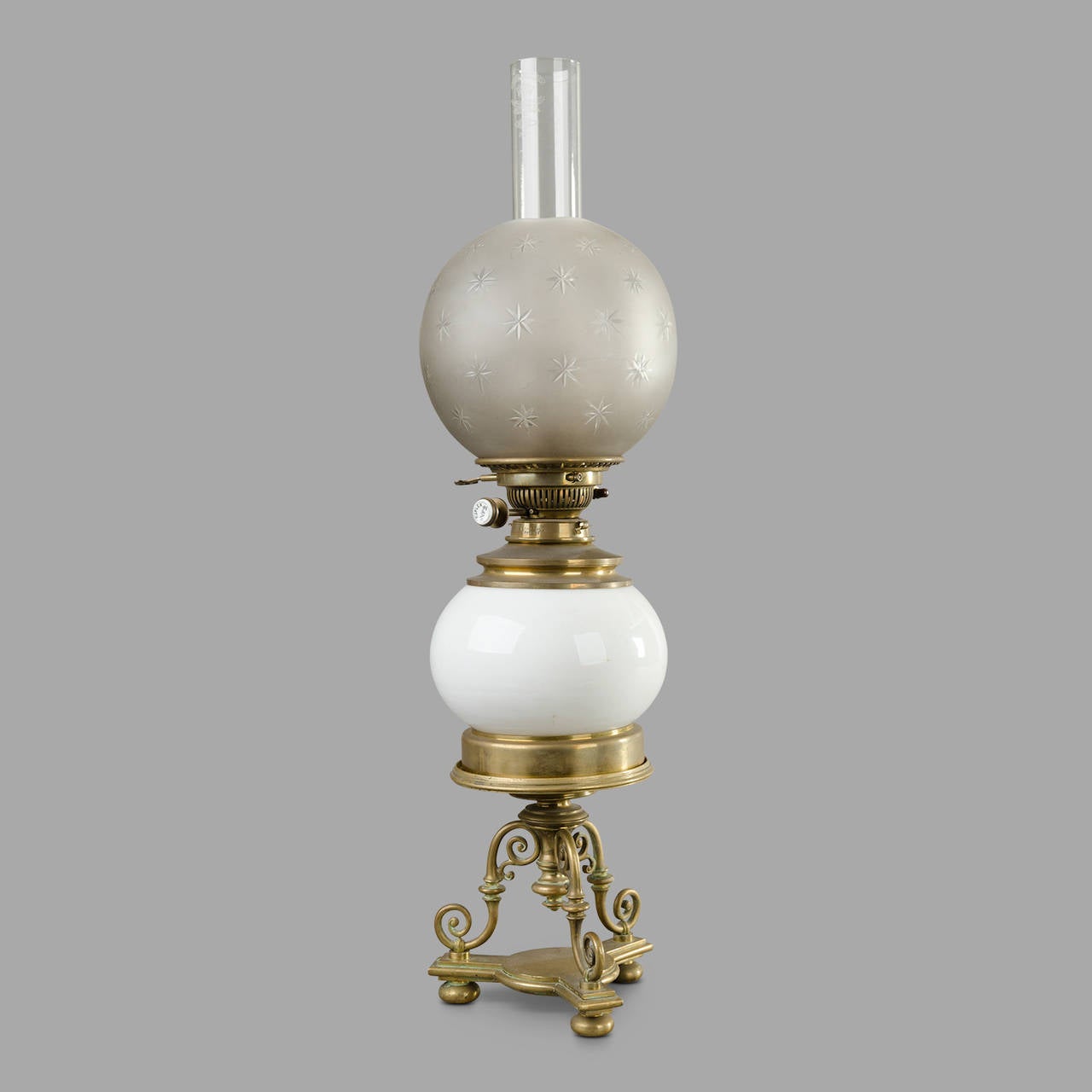 Large late 19th century tripod petrol table lamp. White ceramic reservoir on a brass base. Ground glass with engraved stars.

'Système Duplex n°2.'

Lamp total height: 70cm.
Globe diameter: 19 cm.

In petrol working order but it can be wired