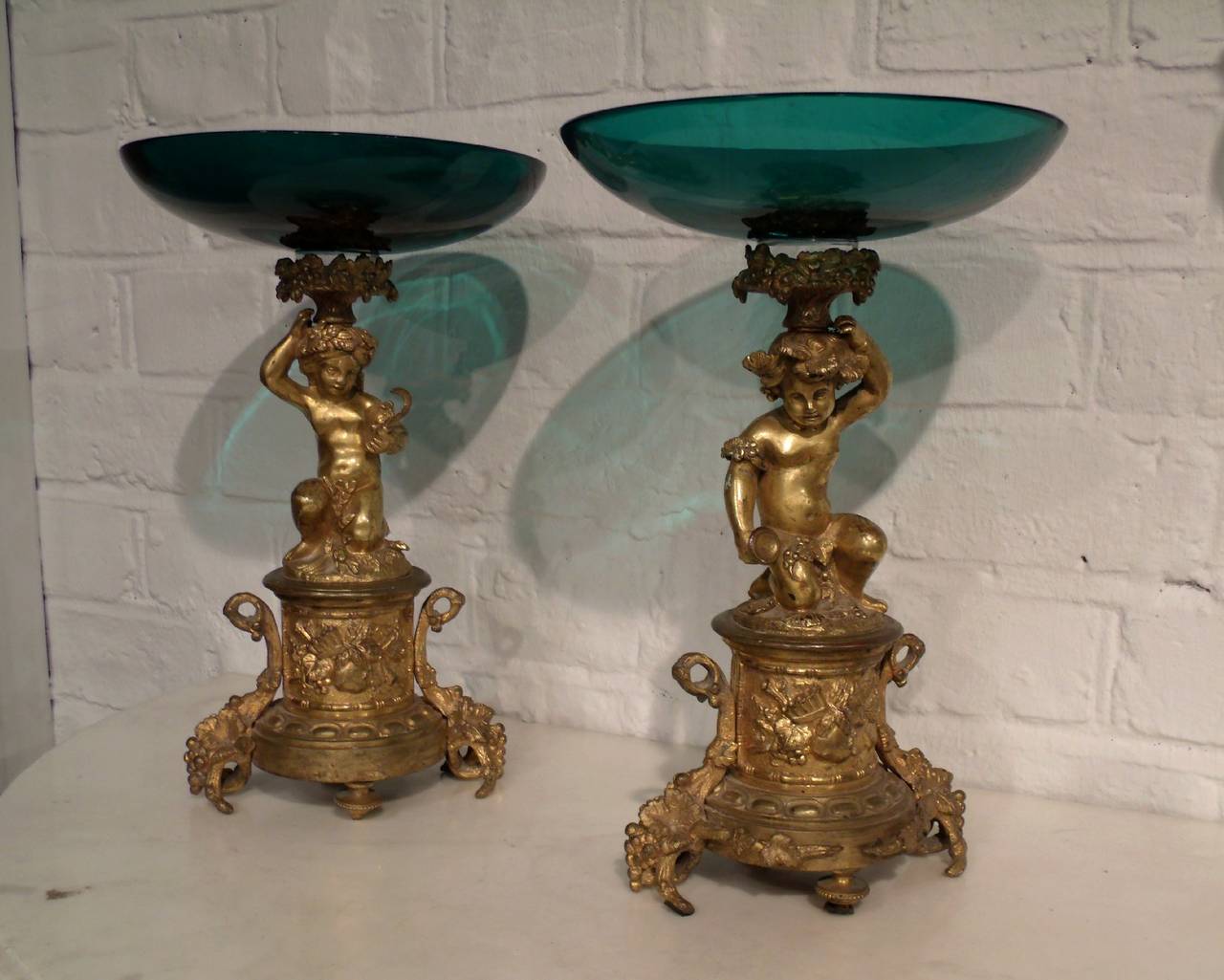 This beautiful pair of French ormolu and glass tazzas, circa 1860, feature a striking blue green glass pair of dishes on top of poising cherubs resting on very detailed bases. The dishes measure 7 ½ in – 19 cm in diameter and Stand 11 ¾ in – 30 cm