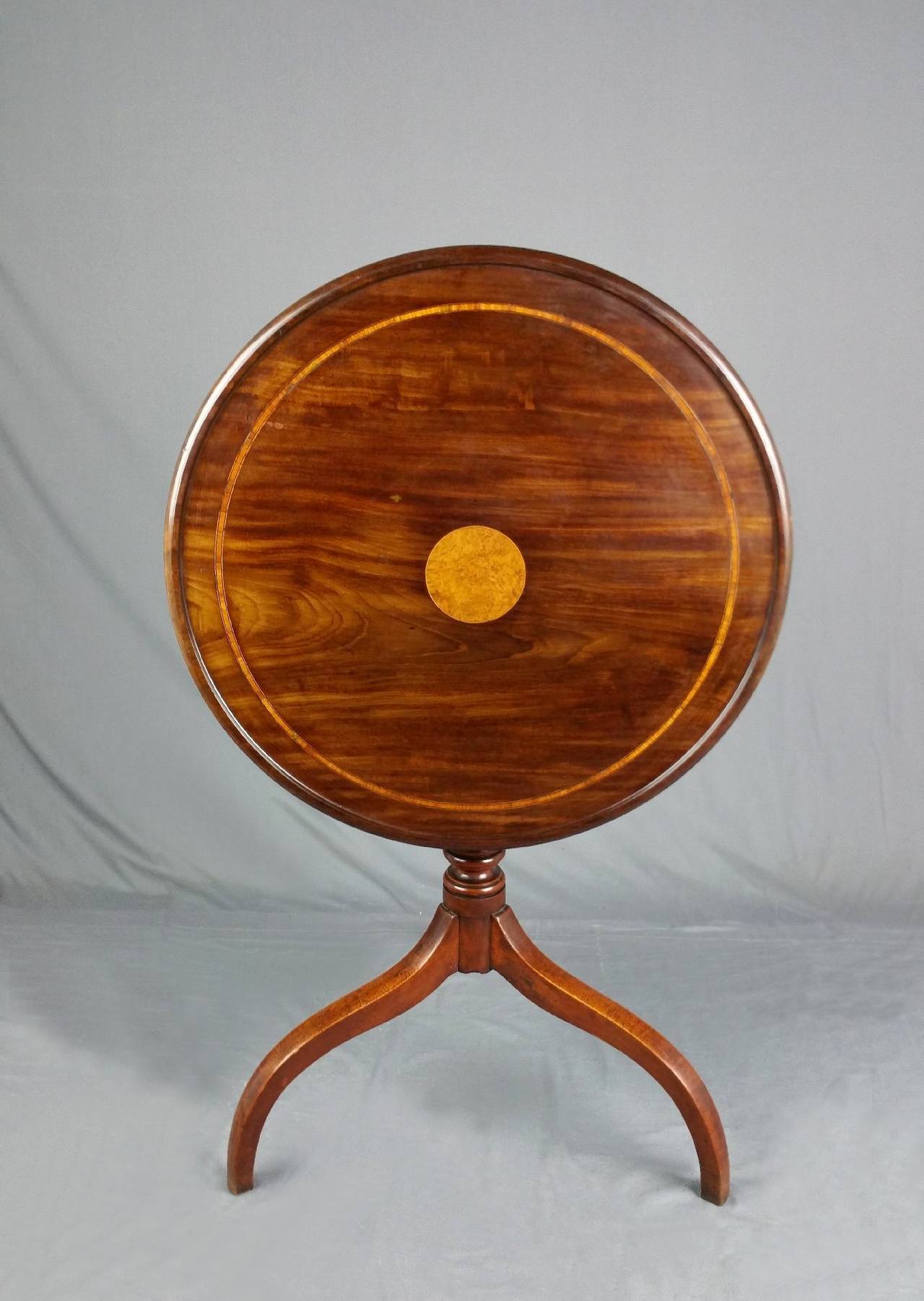 This very attractive George III round tilt top mahogany table features a satinwood center circle with a cross banded outer ring border. The table stands on a tri pod cabriole leg base with a turned column support. It measures 25 in – 63.5 cm in