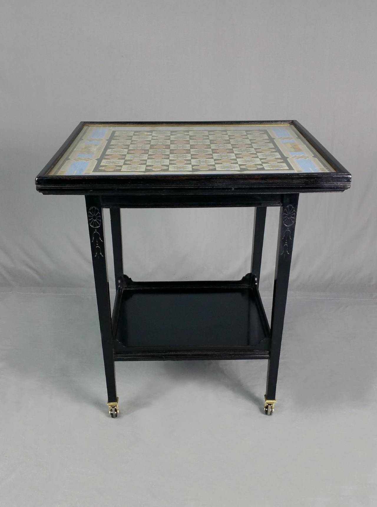 This rare and unusual Victorian two-tiered chess table has an ebonized finish with an outstanding and delicately detailed design. The table stands on square tapered legs, finished with brass mounts and ceramic castors. The top measures 24 ½ in –