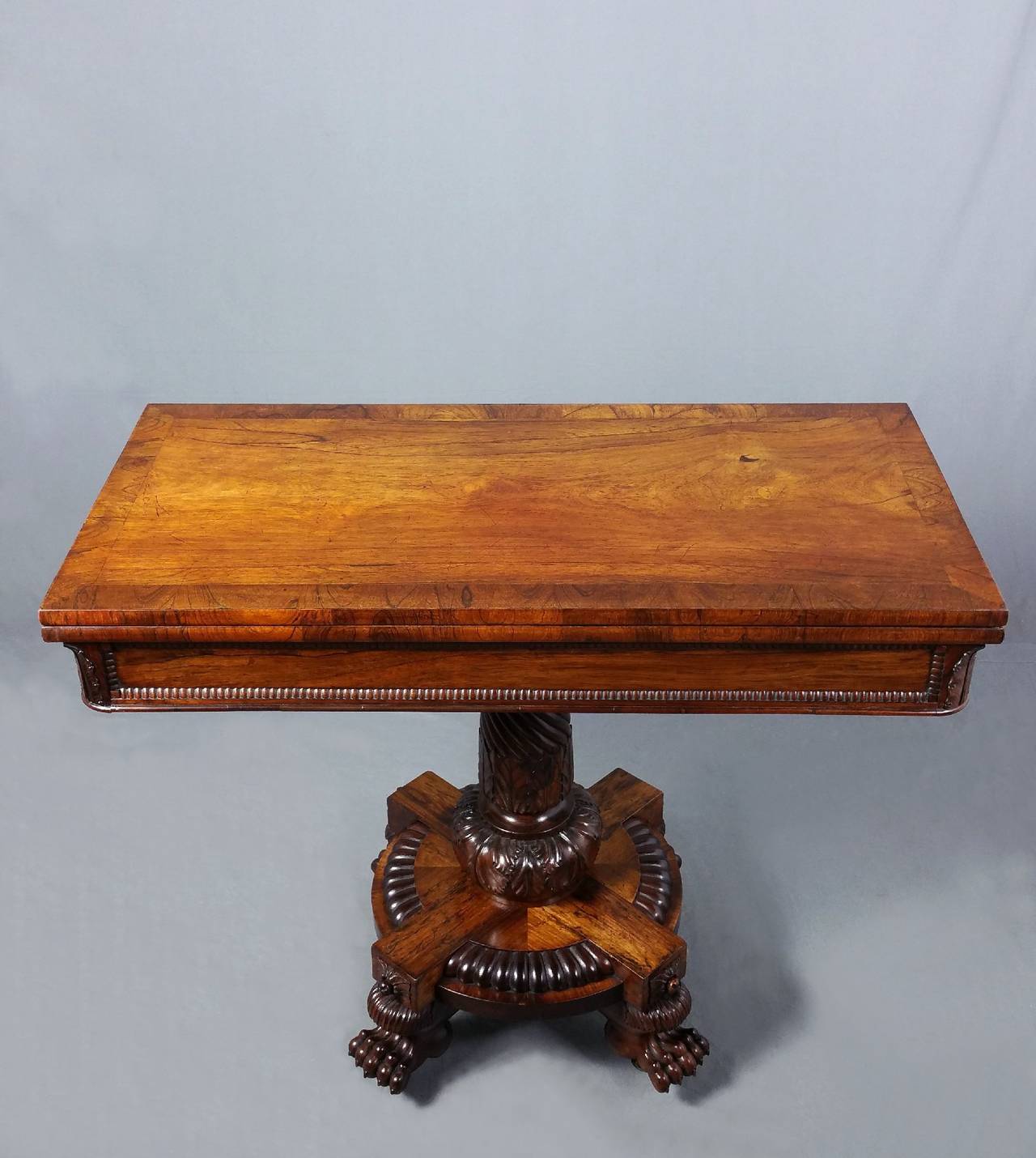 This superb and rare Regency rosewood card table features a beautifully patinated top with a wide cross banded border and rounded corners on the apron that are finished with a carved leaf design. The table is supported on an ornately cut pedestal