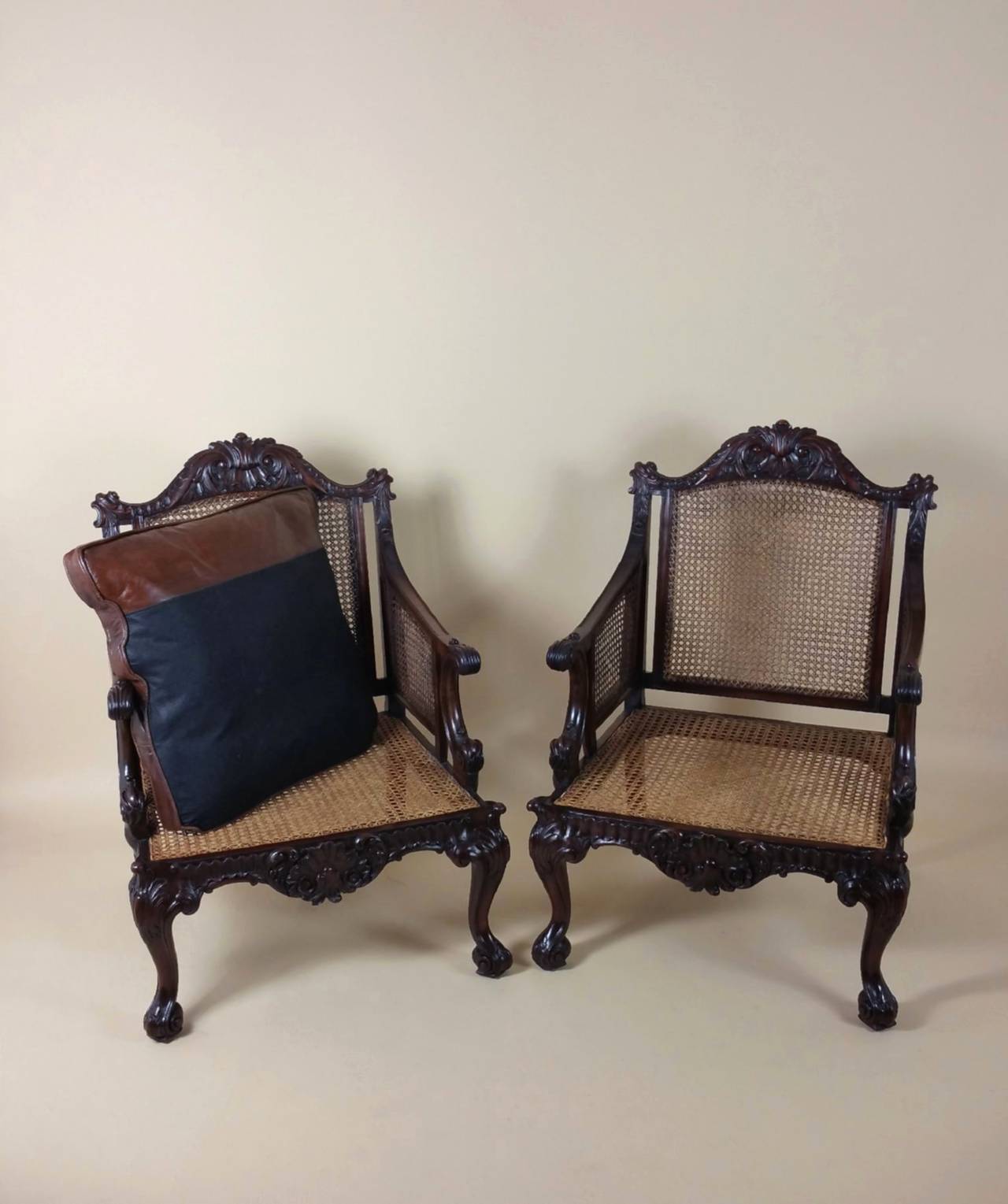 A superb quality pair of Georgian style carved mahogany library chairs with shaped and fitted separate leather seat cushions. The chairs feature a cane seat and back with ornate carvings of C- scrolls and shells on cabriole front and swept back