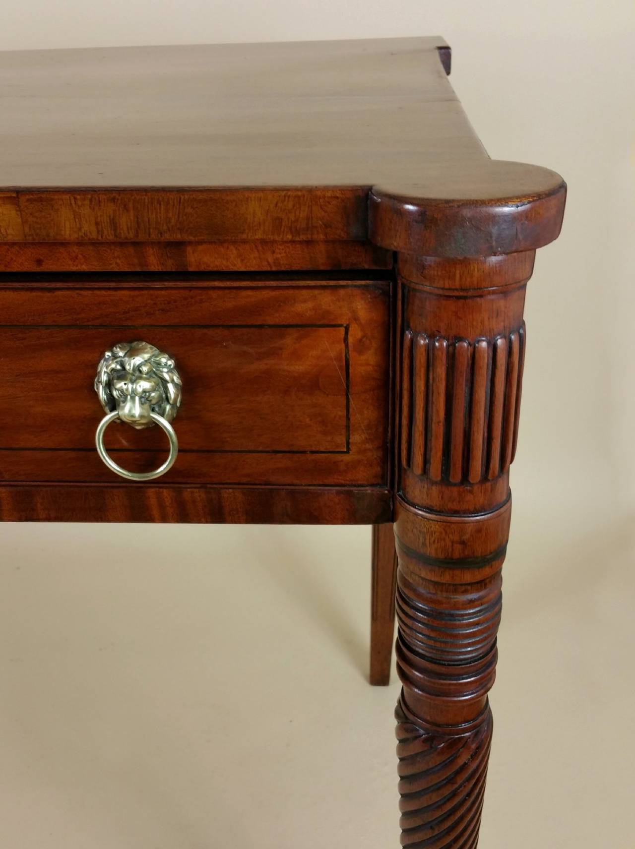 A very well proportioned and handsome Regency mahogany serving table that features a breakfront design with 3 top drawers. The table displays brass inlaid decoration with lion head ring drawer pulls and escutcheons, and is supported on front rope