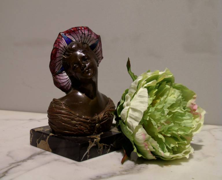 This lovely bronze and enamel Art Nouveau bust of a young maiden stands on a black marble square base and features a very detailed and colorful enameled hat in the shape of a flower. The bronze stands 5 ½ in – 14 cm in height, with a base
