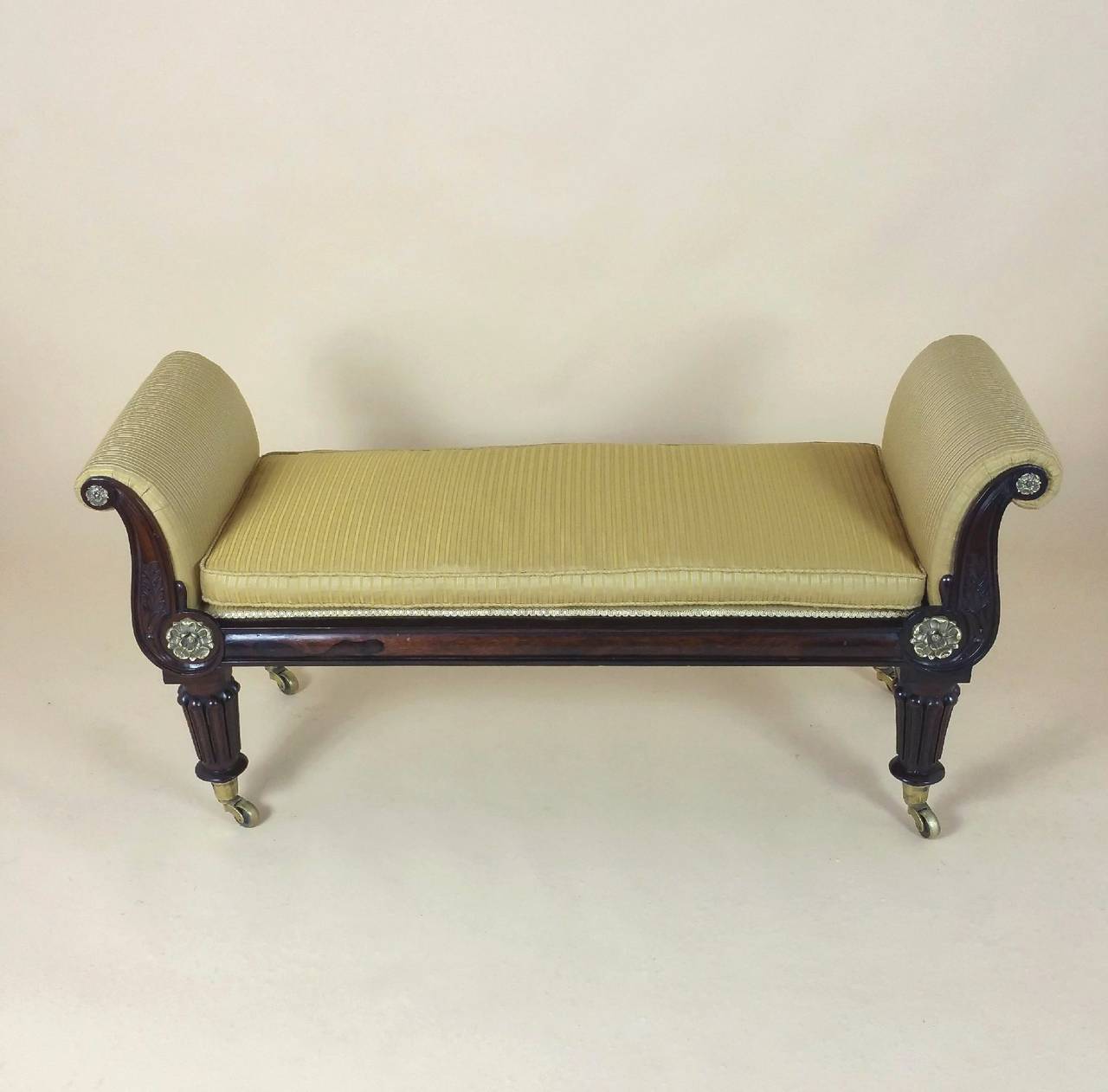 This elegant early 19th C. Rosewood window seat has detailed brass mounts and carved decoration, standing on Carved fluted legs and well-proportioned sized brass castors. The window seat is upholstered in a yellow gold ribbed patterned silk, with a