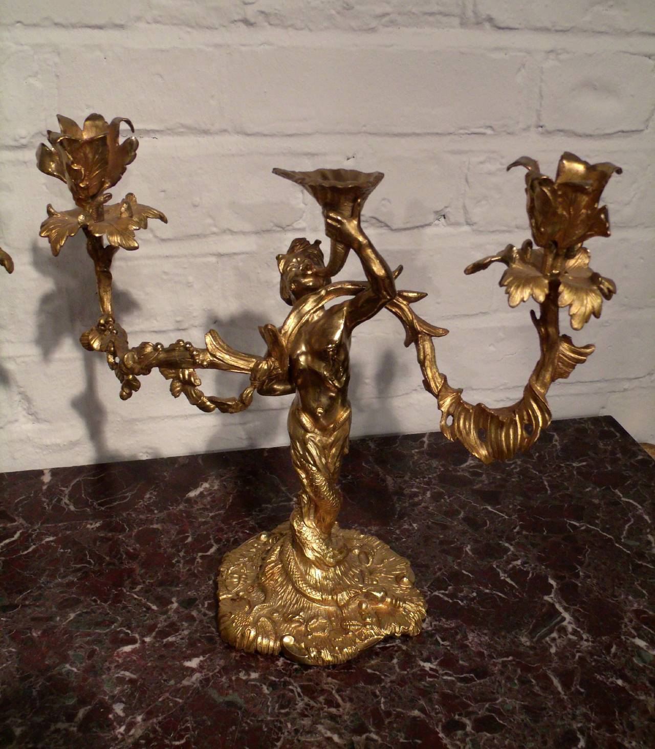 A very ornate and detailed pair of French ormolu double branch table candelabras in the form of mermen. The candelabras are stamped with the makers mark and measure 14 in – 35.5 cm wide, 11 ½ in – 29.2 cm high and approximately 6 in – 15 cm deep.