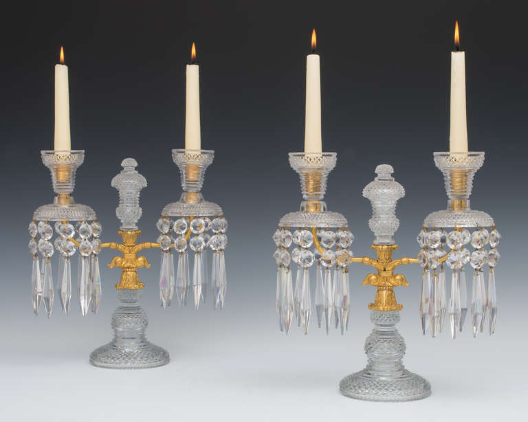 The diamond cut baluster shaped bases supporting an anthemion cast twin branch this surmounted with diamond cut drip pans, step and diamond cut candle nozzles, the candelabras centered by an unusual urn shaped finial, the candelabra draped with
