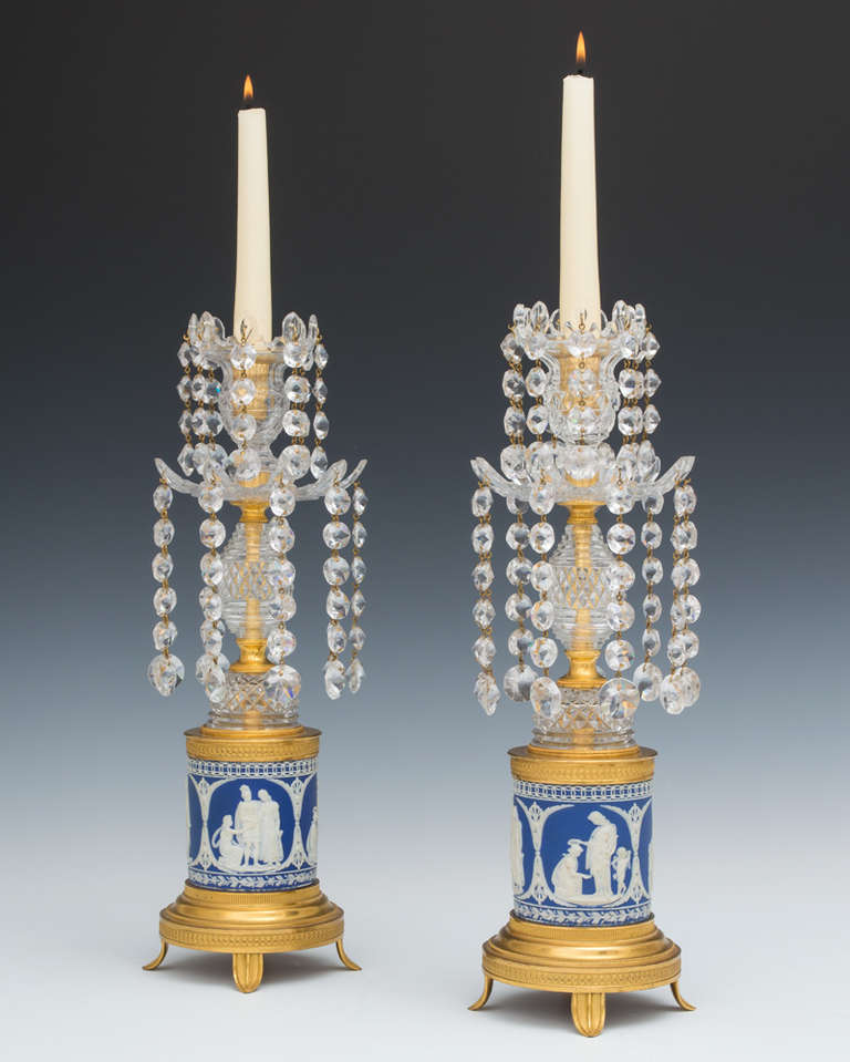 A fine pair of George III period Wedgwood base candlesticks the Wedgwood bases of classic blue and white form, the bases richly decorated with classic Greek scenes the bases surmounted with a step and diamond cut-glass egg this supporting a multi