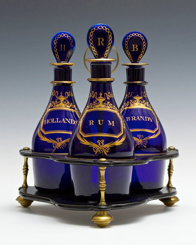 A fine set of blue Georgian decanters with exceptional gilded labels and stoppers fitted in a black lacquer and ormolu stand.
Decanters: Height 9 1/4in (23.5cm). Width 3 1/5in (9cm)
Decanters in stand: Height 10 3/8in (26.5cm). Width 9 1/2in (24cm)