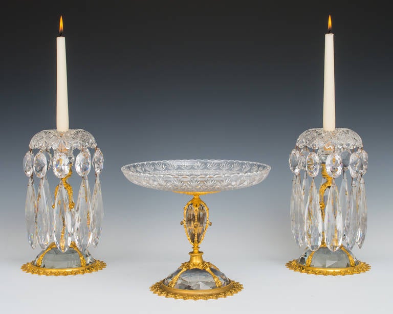 A superb quality pair of ormolu mounted cut glass candlesticks with a matching comport the finely chased ormolu bases surmounted with a lapidary cut glass dome the central lapidary cut glass tear drop also finely mounted with ormolu the turn over