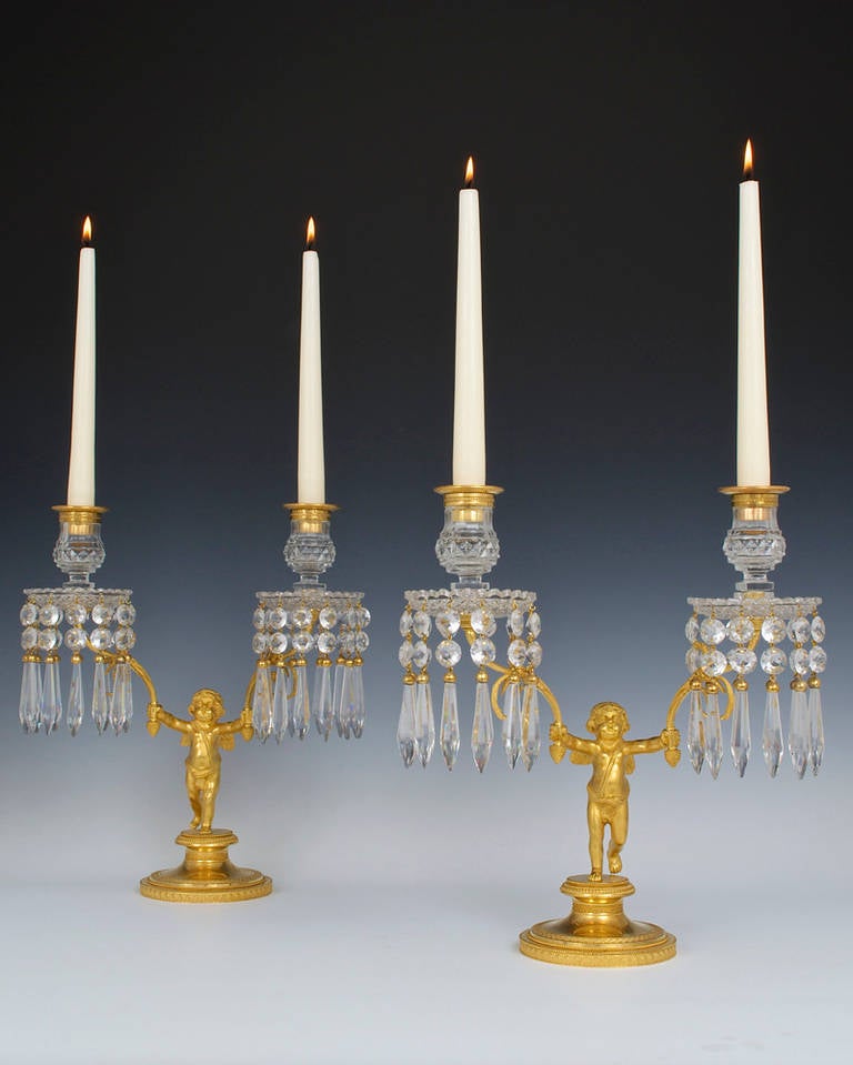 An exceptional pair of English Regency period cut-glass and ormolu two-light candelabra the mercurial gilt bases are decorated with athenaeums within a archway, ball bead, basket weave and bell flower knurls of the finest quality the base supporting