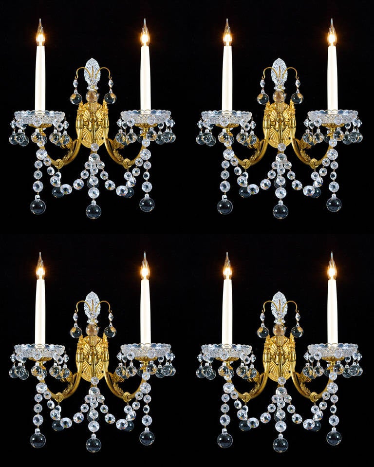 A superb set of four cut-glass, brass lacquered mounted two light wall lights by Perry & co. the oval fan and bead decorated back plates are supporting reed and rosette decorated candle arms terminating with drop hung scallop edged diamond cut drip