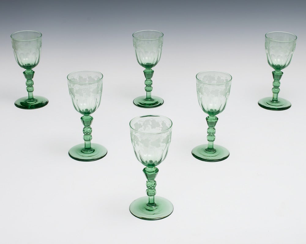 A set of early Victorian green wine glasses on plain foot with unusual facet cut stems supporting a flute cut bowl with engraved fruit and vine.