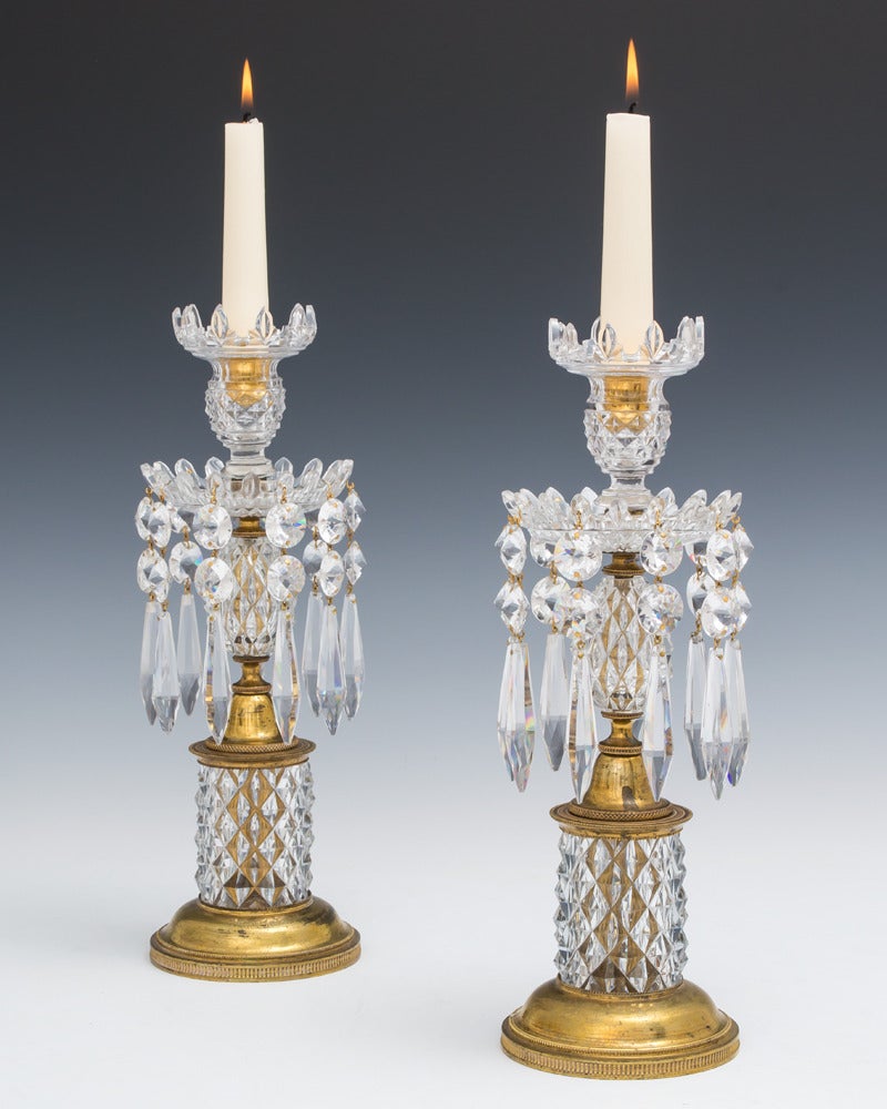 Ein Paar Regency-Kerzenhalter, deren fein gerändelte, vergoldete Basen diamantgeschliffene Glastrommeln tragen. Diese tragen diamantgeschliffene Glaseier, die mit Van-Dyke-Pfannen und Düsen enden, die mit doppelspitzigen Spangles und