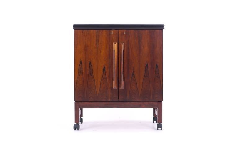Made in Norway circa 1970s, this expandable rosewood bar cart has a durable black laminate top, rosewood exterior and interior and retains the two original keys which lock the cabinet when closed and lock the expanded top to the cabinet when open. 