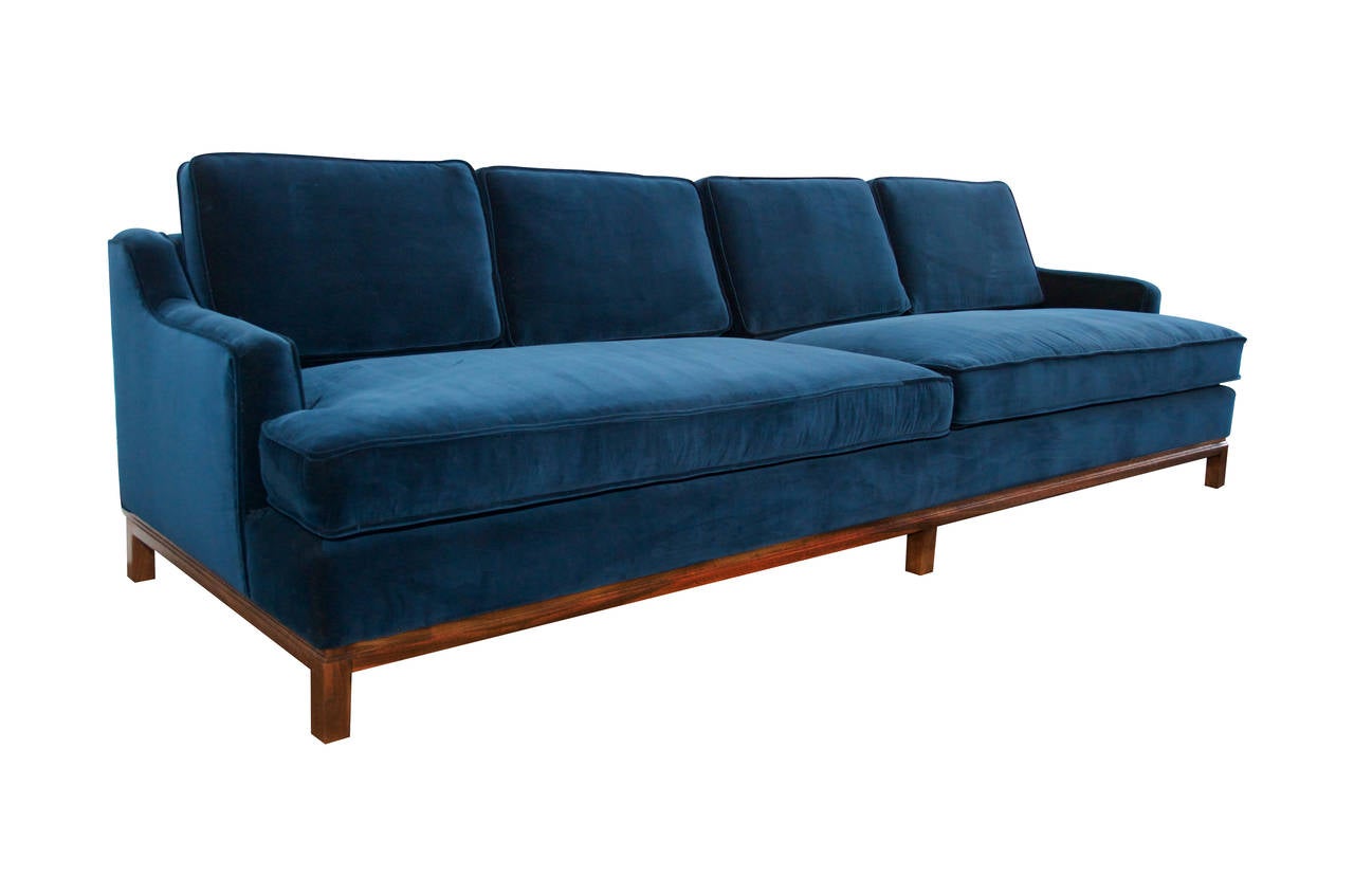 Low and sleek sofa in the manner of Dunbar, 1960s. Walnut base, re-upholstered in inky blue cotton velvet.