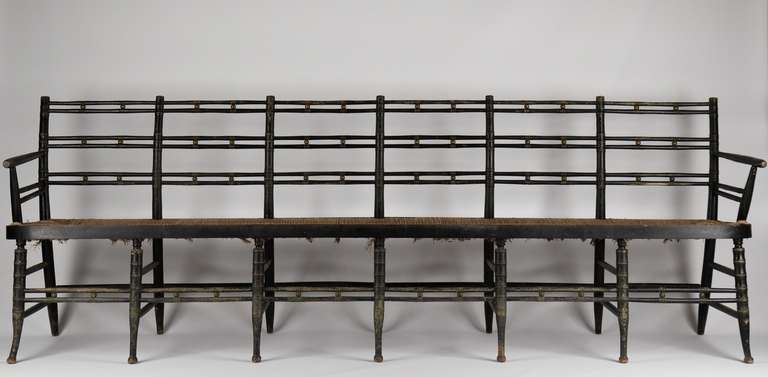 This fine painted bench with six chairbacks over fourteen legs is a work of art in the Sheraton taste, probably c. 1820-40. The design, particularly in the legs, closely conforms to the sentiments of Hitchcock chair designs (c. 1825-50) of the