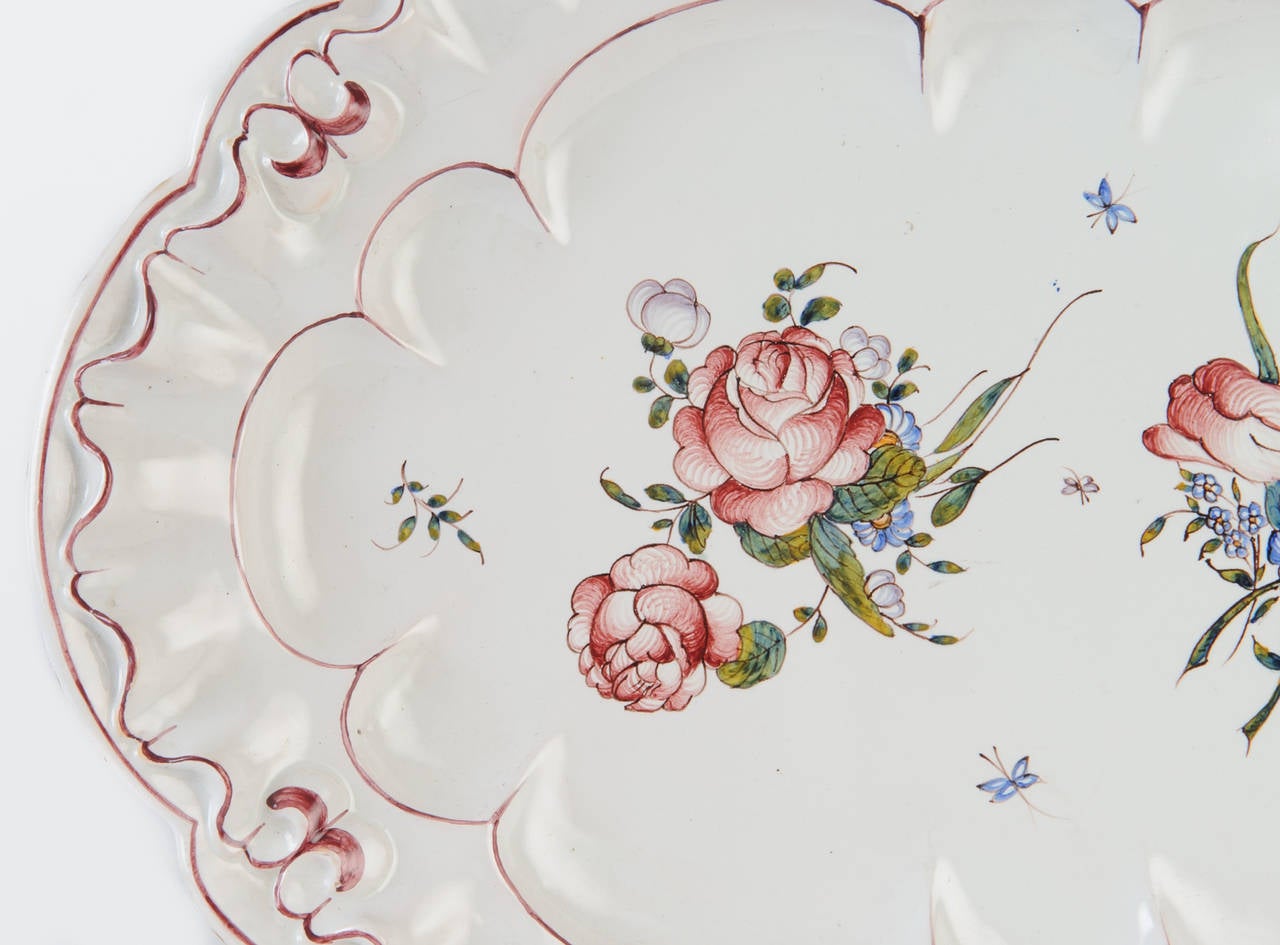 This faience platter with bright floral motif and undulating edge is in very good condition. The hand painted design is beautifully executed with fine detail. 
The tulips, roses, and small bluebells with the rose pink edge detail on white