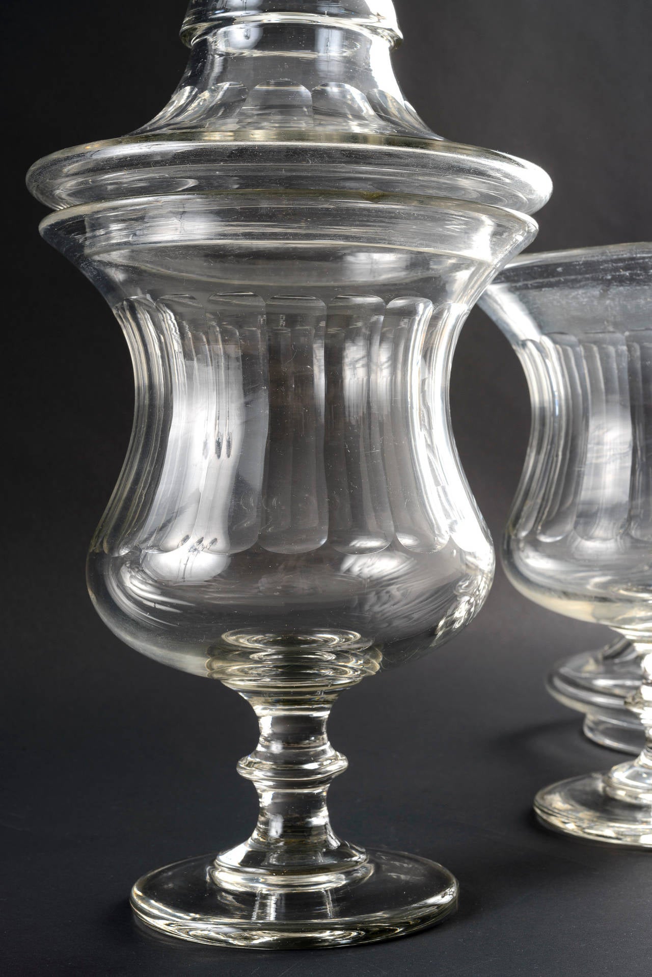 This pair of French goblet shape apothecary jars with covers are a matched set. The large-scale gives a formidable presence to the pair. The ringed base of the jar is in good scale with the finial of the cover. There is a minor chip on each of the