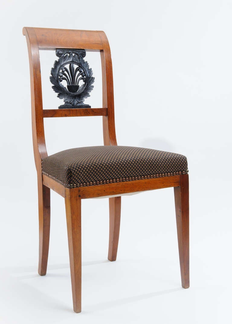 This is a handsome pair of Empire side chairs with carved wood laurel wreath and palmetto medallion on the center back. The front legs are tapered. The rear legs are scabbard shaped and indicative of the period. The lines of the chair are simple and