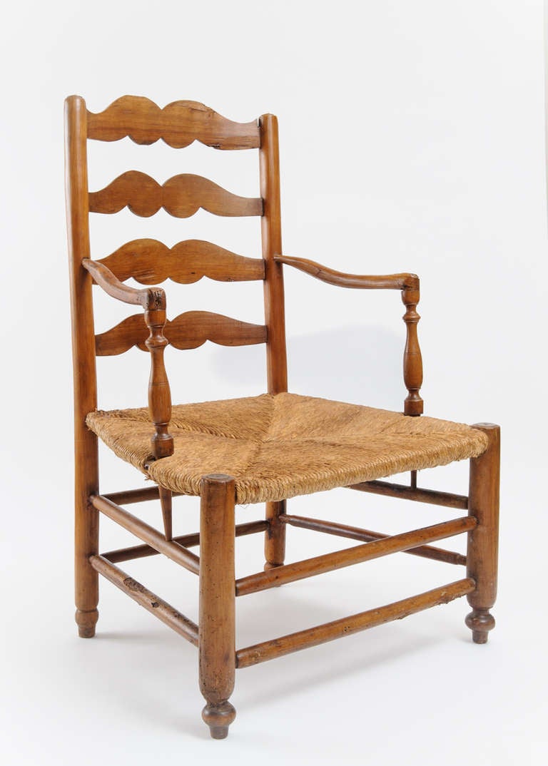 This is the quintessential French ladder back chair.  The shape of the ladder back and arms of this chair is characteristic of furniture from the Southwest region of France.  The ladder back has double scroll slats.  The delicate arms of the chair