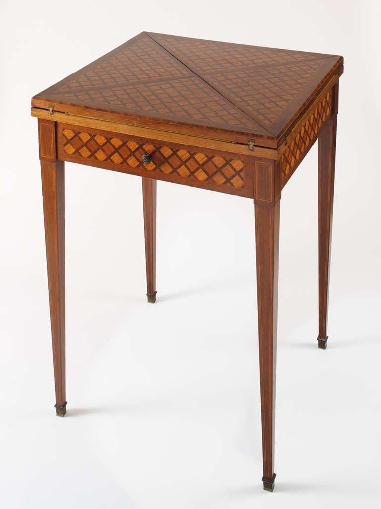 This game table has fine parquetry and inlay of mixed woods suggesting the artisan work of a Parisian ebineste. The table has a veneer edge and is chamfered. The delicately tapered legs have fine inlay and bronze foot caps. The table has one drawer.