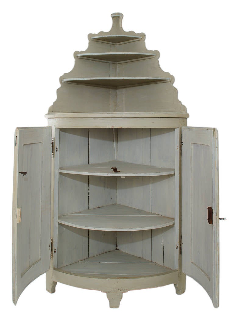 This 18th century painted cabinet has a bow front and is in two parts. The base has a raised panel with generous moldings. The original Directoire hardware includes the hinges, lock, diamond shape cover plate, and key. The upper shelf unit has a