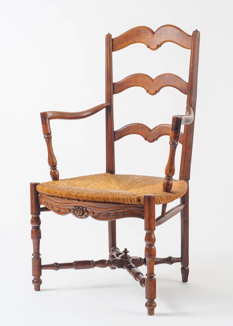 This 19th century country ladder back armchair, Fauteuil de Paille. Has a refined execution. The floral and leaf detail on the seat apron is typical of the period. The chair arms are flared and turned with a point support to the stretcher. The
