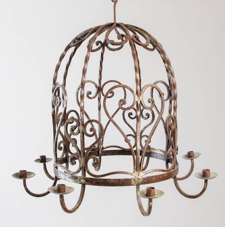Lustre inhabituel en fer en forme de cage à oiseaux avec huit bougies. Le motif du cœur et de la volute est répété sur l'ensemble. L'échelle est parfaite pour un plafond voûté.
