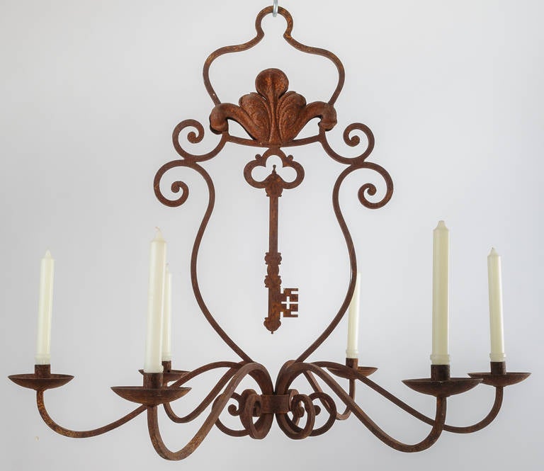 Charming chandelier with centre key and scroll motif. Chandelier is not electrified but has six candle cups. It has a rusted iron finish.  It is drilled for electrical wiring if that should be the choice of illumination.