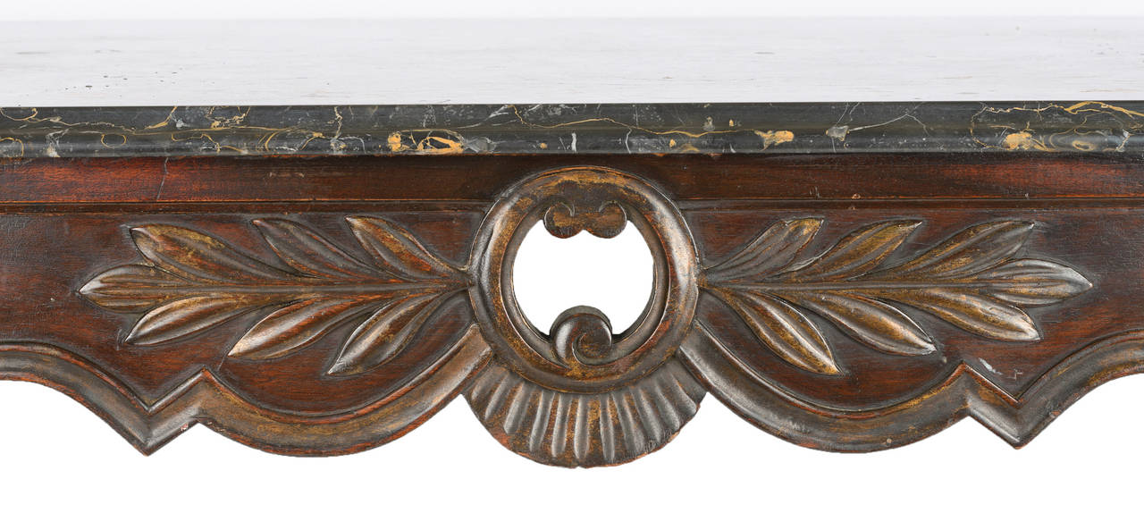 This heavily carved Louis XV table still shows some of the original gilding. The center apron has an open center with scrolls, acanthus leaves, and drapery folds. The unbroken line of the horizontal apron and the cabriole legs has a carved thumb