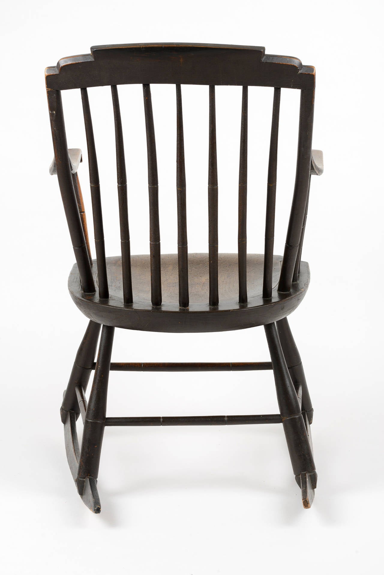 This Windsor rocker is from the Connecticut Valley in New Hampshire.  The step back top sits on tapered and bowed spindles that have decorated notch mid high on the back.  The arms are tapered with a delicate scroll end.  The chair has a spoon seat.
